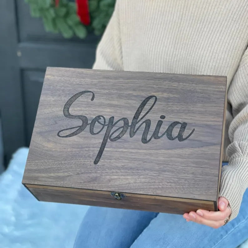 Person holding a wooden box with 'Sophia' engraved on it, against a blurred background.
