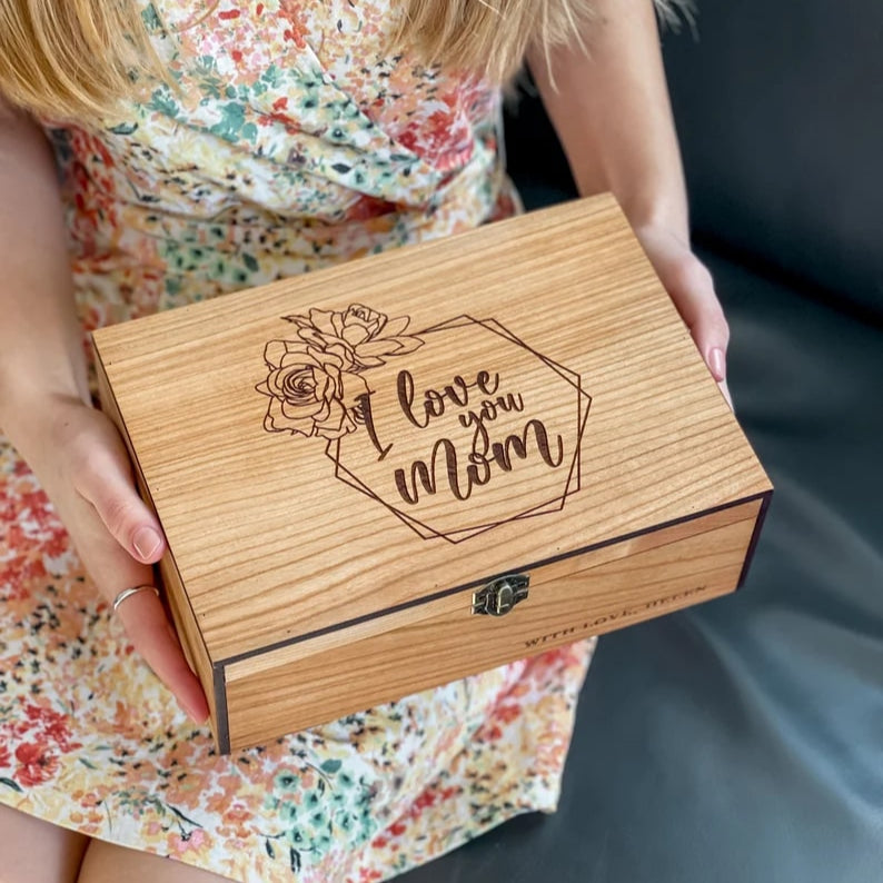 Wooden box with 'I love you Mom' engraving held by a person in a floral dress.