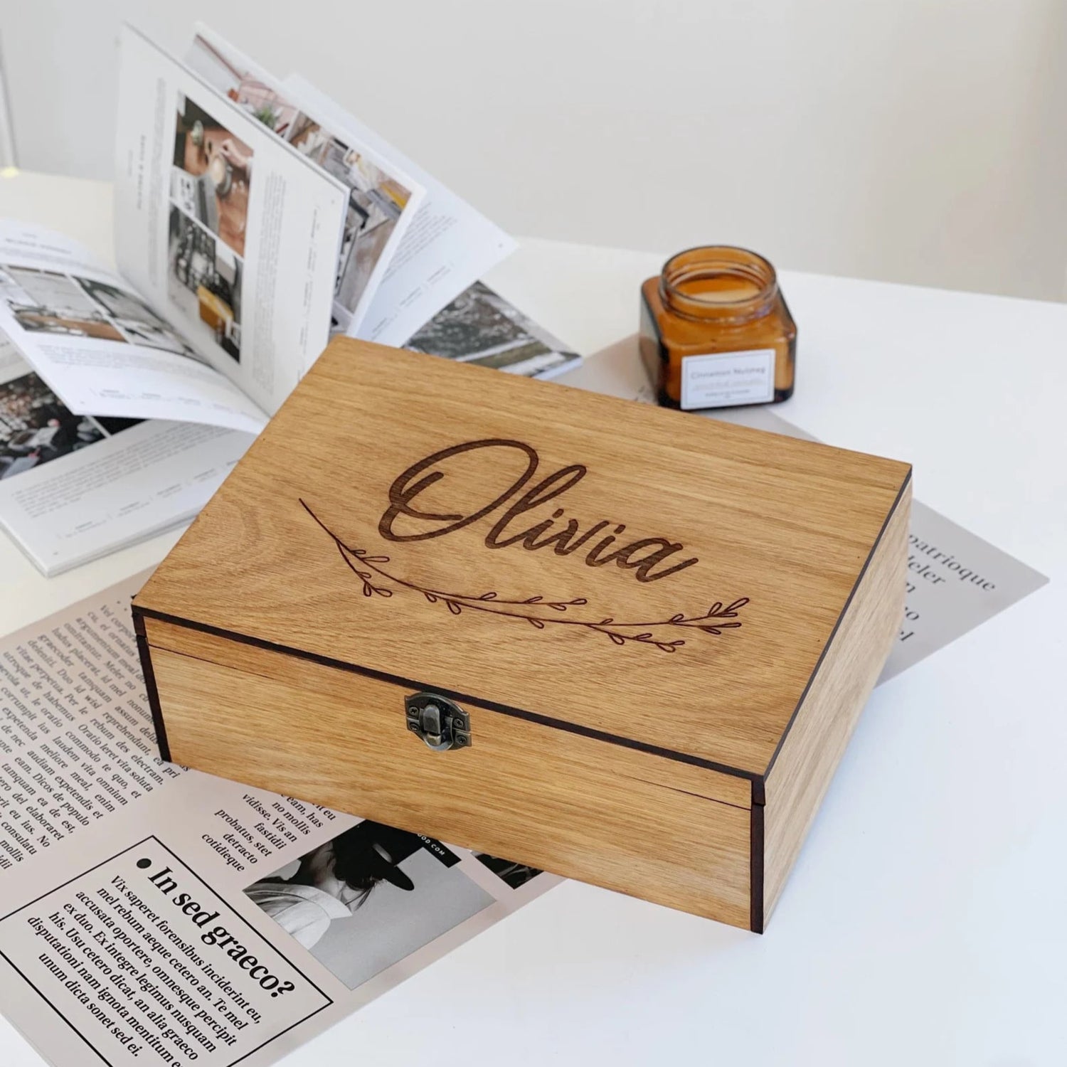 Wooden box with 'Olivia' engraving on a surface with magazines and a candle.