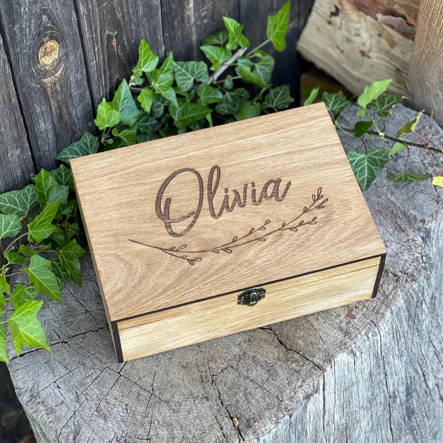 Wooden box engraved with 'Olivia' on a rustic wooden surface with greenery.