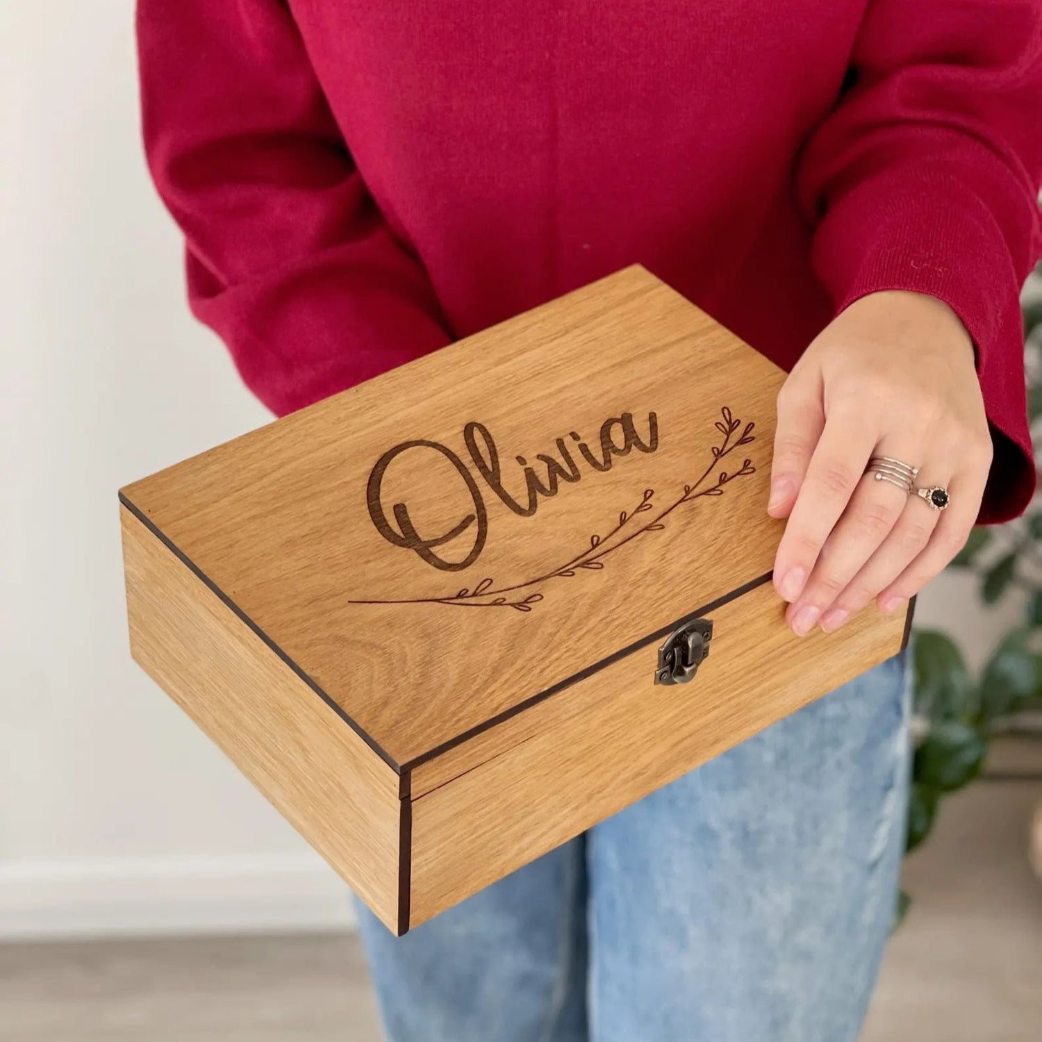 Person holding a wooden box with 'Olivia' engraved on it, wearing a red sweater and blue jeans.
