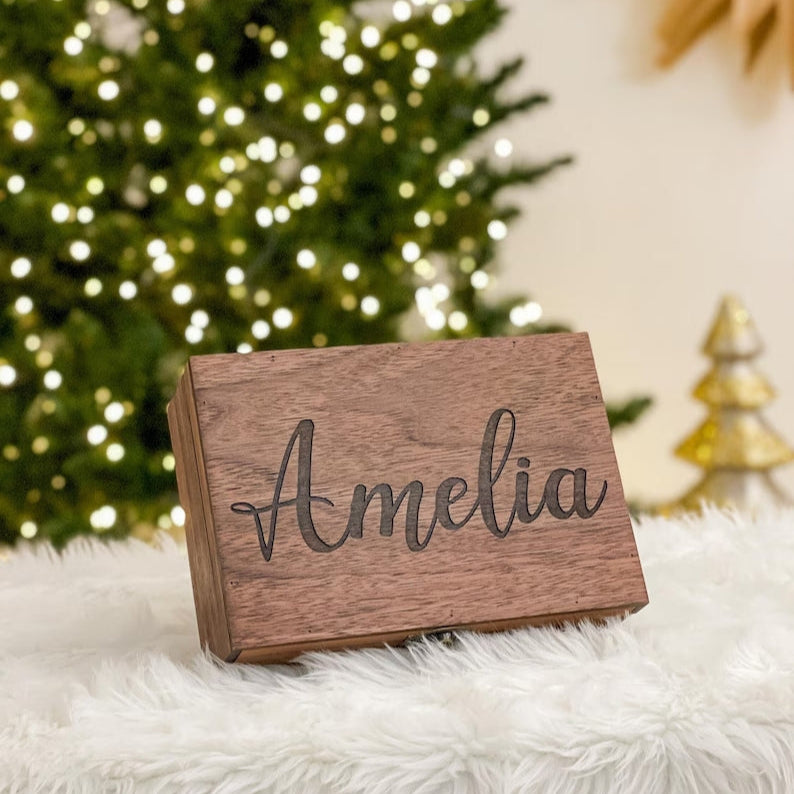 Wooden name plaque with 'Amelia' engraved, placed on a fluffy white surface with a Christmas tree in the background.