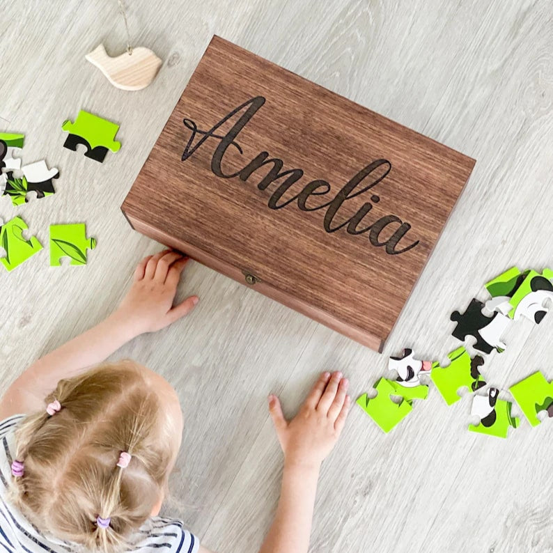 Child playing with a wooden box labeled 'Amelia' on a wooden floor.