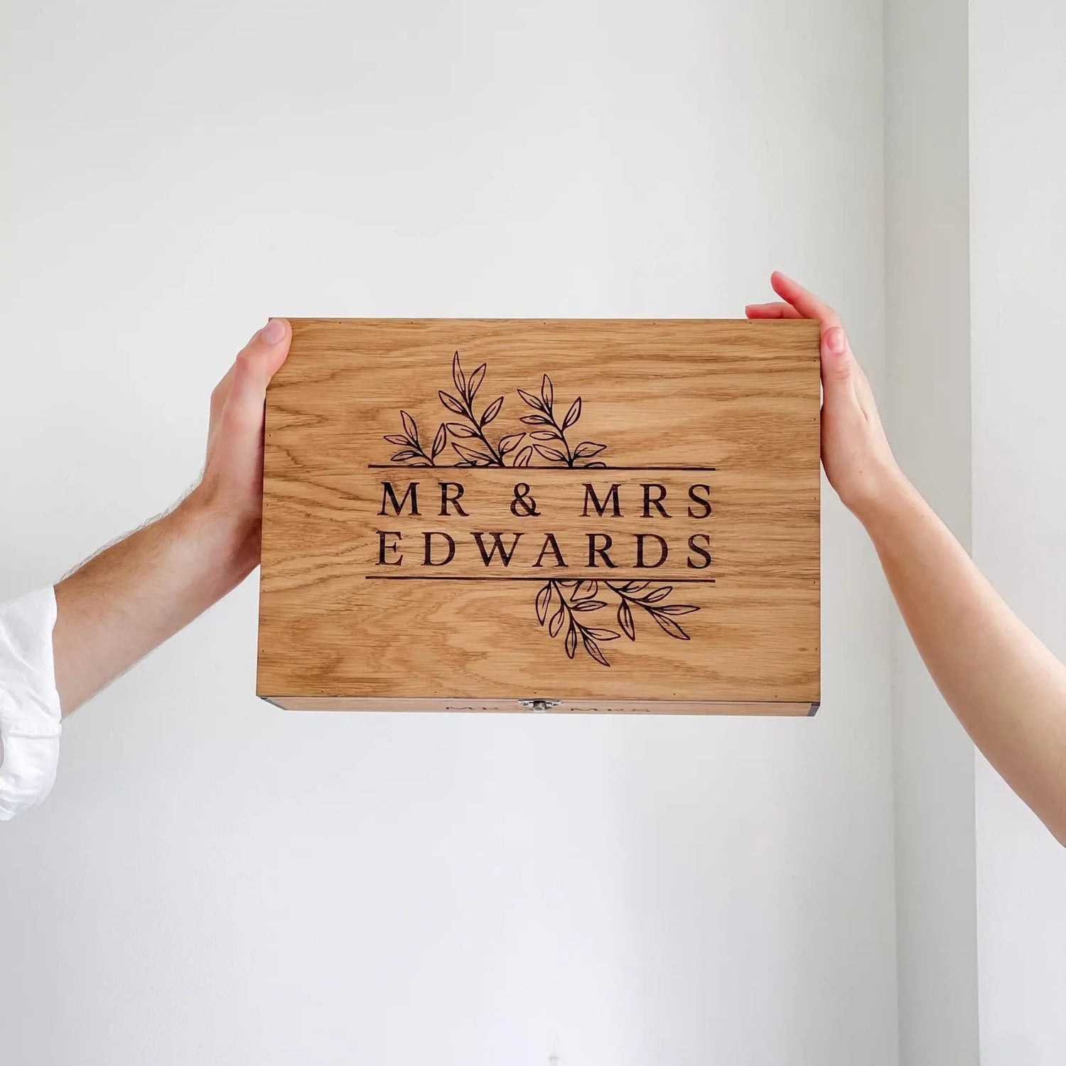 Wooden cutting board with 'MR & MRS EDWARDS' engraving held by two hands against a white background