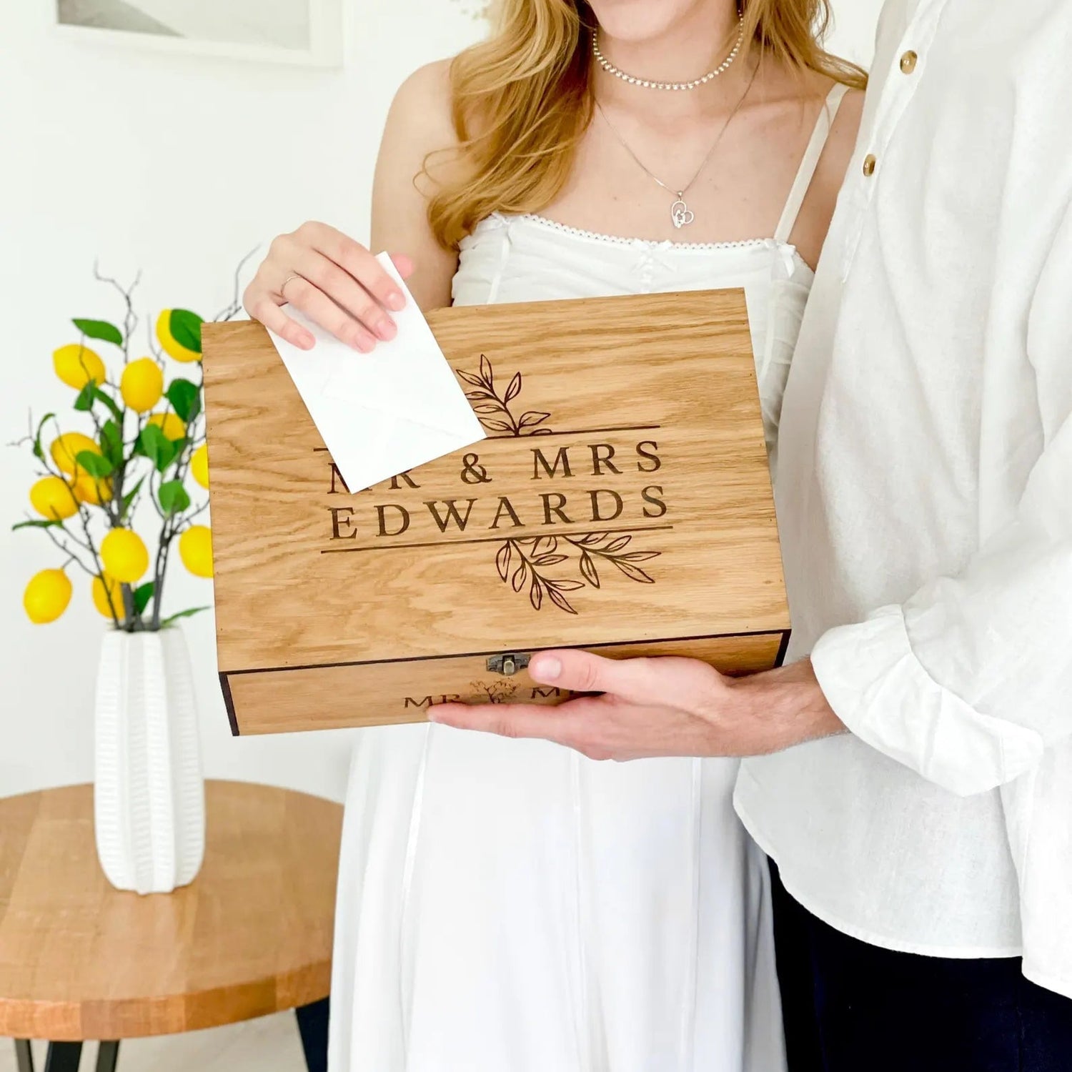 Two people holding a wooden box engraved with 'Mr & Mrs Edwards' in a home setting.